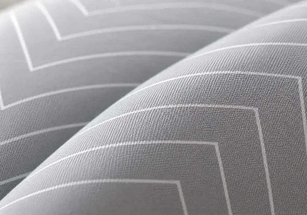 Macro sur le tissu gris à fins chevrons blancs du coussin, lumière rasante révélant le tissage